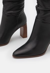 Bottines en cuir noir avec bout pointu, design décontracté et talon bloc en bois. Texture lisse, détails de couture minimaux.