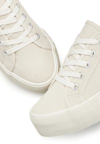 Beige kanvas tossud, millel on ümar nina, valged paelad ja hõbedased silmad, tekstureeritud kummist tallad ja peened õmblusdetailid.