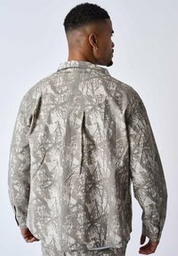 Camisa overshirt gris con un patrón, que presenta un corte holgado, una textura suave y un cuello puntiagudo con un diseño abstracto multicolor.