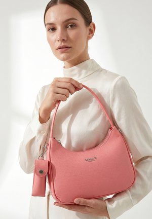 Vrouw in witte blouse houdt een roze handtas met afneembaar tasje vast, merk "DIANA&CO FIRENZE" zichtbaar aan de voorkant van de tas.