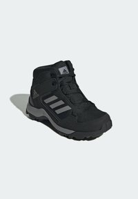 Chaussure de sport montante noire avec tige synthétique, finition texturée, accents gris et semelle en caoutchouc à rainures ; équipée d'une fermeture à lacets et d'un logo.