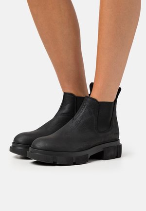Bottines en cuir noir avec panneaux élastiques sur les côtés, surface texturée et semelle en caoutchouc épaisse. Design minimaliste sans quincaillerie visible.