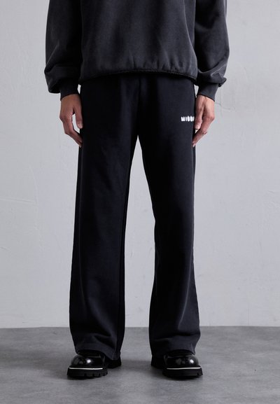 Pantalons de survêtement noirs en tissu doux, dotés d'une coupe décontractée et d'un accent logo blanc. Assortis avec un sweat à capuche ample de couleur sombre.