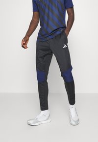 Schwarze Sporthose mit marineblauen Akzenten, schmaler Schnitt, elastischer Bund und drei weißen Streifen-Logo am linken Bein.