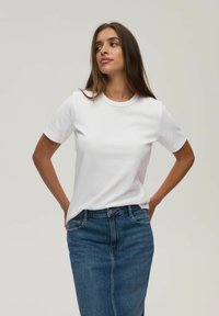 Biała koszulka z okrągłym dekoltem i krótkimi rękawami, zestawiona z dopasowaną niebieską spódnicą dżinsową. Gładka faktura materiału, casualowy kroj.