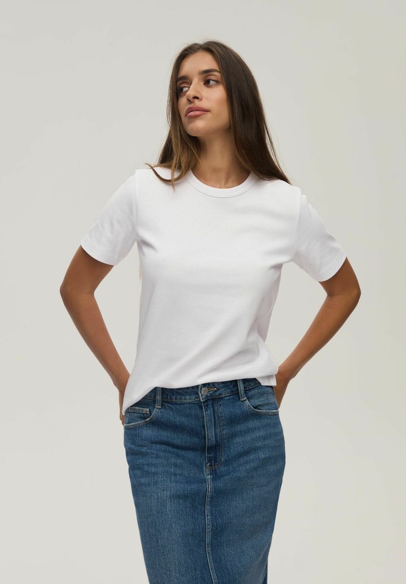 Biała koszulka z okrągłym dekoltem i krótkimi rękawami, zestawiona z dopasowaną niebieską spódnicą dżinsową. Gładka faktura materiału, casualowy kroj.