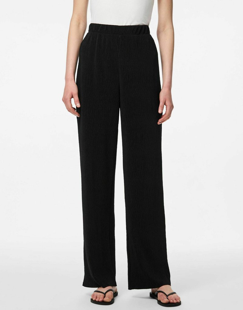 Pantalons larges noirs avec un tissu texturé et une taille élastique, présentant une coupe décontractée et des lignes verticales subtiles.