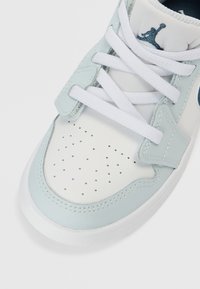 Ανοιχτό μπλε και λευκό αθλητικό παπούτσι με διατρημένη περιοχή δακτύλων, υφασμάτινη γλώσσα, λευκούς κορδόνια και μπλε λογότυπο στο πίσω μέρος. Απαλή μίξη δέρματος και υφάσματος.