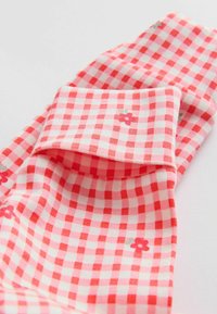 Tissu vichy rouge et blanc avec de petites impressions de fleurs rouges, plié pour montrer le motif et la texture sur un fond clair.