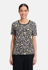 T-shirt à manches courtes et col rond en tissu doux, présentant un imprimé abstrait noir, jaune et vert sur un fond beige.