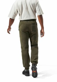 Olivgrüne Fleece-Jogginghosen mit elastischen Bündchen, ausgestattet mit Seiten- und Gesäßtaschen, kombiniert mit schwarzen strukturierten Schuhen und gemusterten Socken.