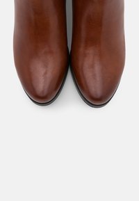 Botas de tobillo de cuero marrón con un acabado suave, punta afilada y un sutil detalle de costura. La suela de goma negra ofrece contraste y durabilidad.