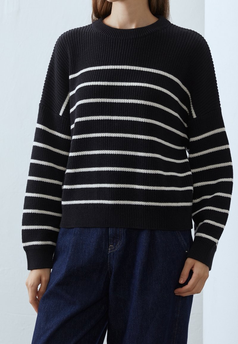 Pull en tricot à rayures noir et blanc avec une texture côtelée et un col ras du cou. Manches larges, coupe décontractée et ourlet contrastant.
