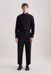 Camicia nera con bottoni e colletto dritto, abbinata a pantaloni neri a vita alta e scarpe nere con lacci. Tessuto liscio e vestibilità su misura.