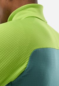 Close-up of a person wearing a two-tone textured shirt with a lime green upper section and dark teal lower section.