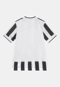 Valkoinen paita, jossa on mustat pystysuorat raidat hihoissa ja musta-valkoiset vaakaraidat helman kohdalla. Lyhythihainen malli.