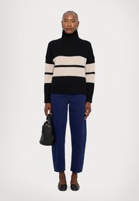 Black and cream striped knit turtleneck sweater, paired with blue straight-leg jeans and black flats, holding a small black handbag.