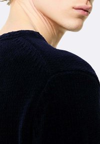 Maglione blu navy lavorato a maglia con un design a trama e scollo rotondo, che mostra un primo piano della spalla e dell'area del collo.