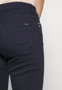 Marineblauwe jeans van denim, met een aangesloten silhouet, ton-sur-ton stiksels en een patchzak met een klein metallic logo-detail.