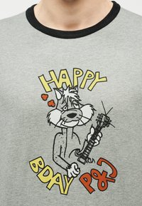 Γκρι πουκάμισο με μαύρο γιακά που απεικονίζει μια καρτούν γάτα που παίζει ηλεκτρική κιθάρα με το κείμενο «HAPPY BDAY PQ?» σε κίτρινα και κόκκινα γράμματα.