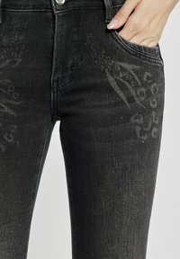 Czarne dżinsy z dopasowanym krojem, lekkimi przetarciami i subtelnymi wzorami graficznymi z przodu.