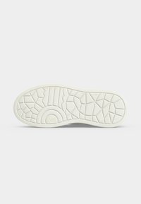 Semelle de chaussure en caoutchouc blanc avec motifs géométriques et circulaires sur un fond clair uni.