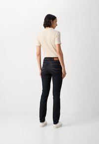 Mörkblå jeans med slim fit, med bakfickor och en brun läderlogotyp. Bärs med en rippad beige topp och vita sneakers.