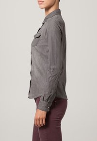 Camicia grigia a maniche lunghe con bottoni, due tasche sul petto, colletto e una vestibilità leggermente sfiancata. Il tessuto sembra leggero e morbido.