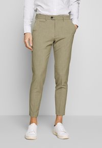 Ljusgröna skräddarsydda byxor med texturerad yta, med knappstängning fram, sidofickor och slim fit, tillsamman med vita sneakers.