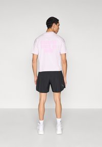 Ανοιχτό ροζ βαμβακερό t-shirt με την επιγραφή "RUNNING STATE OF MIND" σε πιο σκούρο ροζ στο πίσω μέρος, σε συνδυασμό με μαύρο σορτς και λευκά αθλητικά παπούτσια.