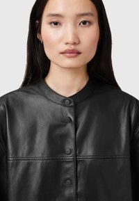Black leather jacket with a round neckline, front buttons, and subtle stitching details. Smooth texture and tailored fit.