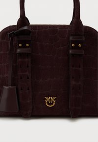 Bordeaux suède handtas met een gestructureerd krokodillenpatroon, dubbele leren banden en gouden hardware met een decoratieve ringaccent.