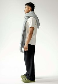 Écharpe grise drapée sur un t-shirt blanc, associée à un pantalon plissé noir et des baskets vertes. Les accessoires comprennent plusieurs bagues sur une main.