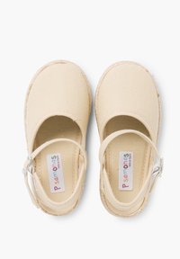 Chaussures Mary Jane en toile beige avec une sangle, un bout rond et un tissu texturé. Présente un bord cousu et une étiquette de marque colorée.