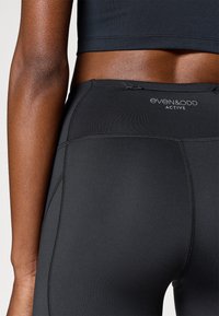 Mallas negras para actividad física con textura suave, cintura alta y detalles de costuras sutiles. El logotipo de la marca es visible.