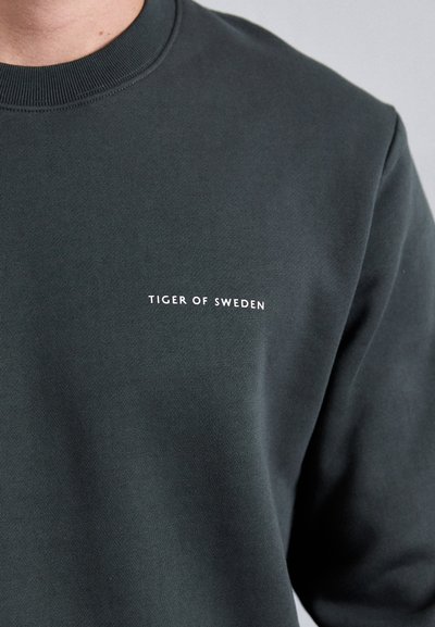 Dark green sweatshirt made of soft fabric, featuring a round neckline and the text "TIGER OF SWEDEN" in white on the chest.