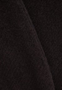 Zbliżenie na czarny materiał teksturowany o miękkiej, puszystej powierzchni oraz zachodzących na siebie fałdach.