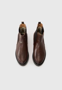 Bottines en cuir marron avec des panneaux élastiques sur les côtés, bout rond et semelle texturée noire, dotées d'une languette à l'arrière.