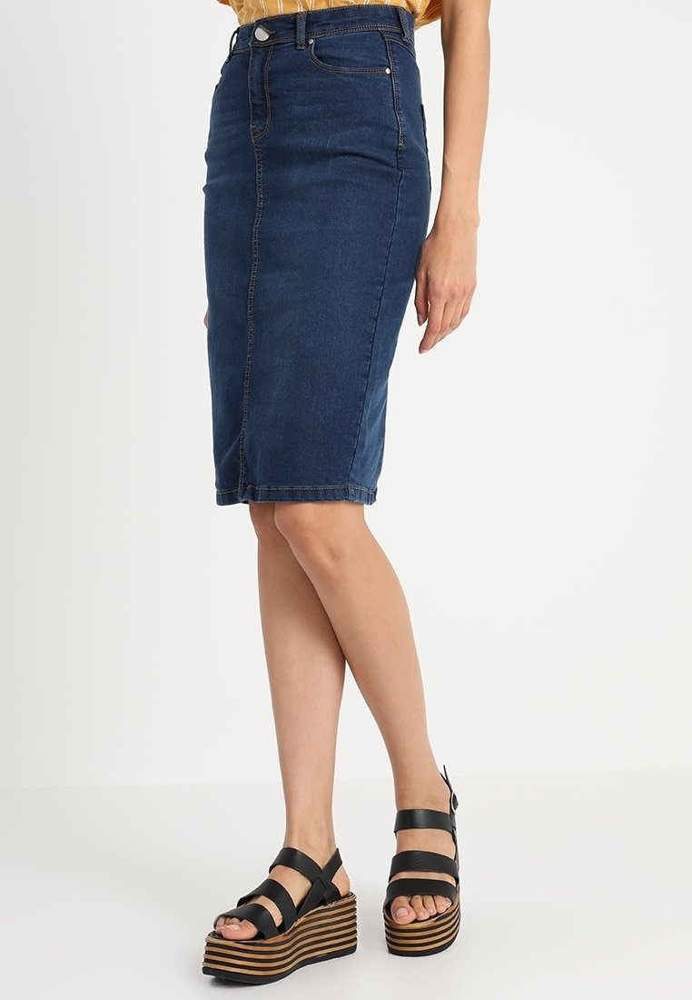 Falda lápiz de mezclilla en azul oscuro con un corte medio. Presenta bolsillos frontales, un diseño ajustado y costuras blancas a lo largo de las costuras.