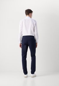 Hvit langermet skjorte med knappemanchetter, kombinert med marineblå bomullsbukser og hvite sneakers. Minimalistisk design, skreddersydd passform.