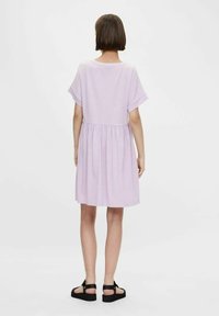 Fioletowa sukienka z krótkim rękawem, z marszczoną talią, miękkiego materiału i luźnym kroju, w połączeniu z czarnymi płaskimi sandałami na jednolitym tle.