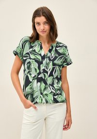 Camicia a maniche corte in tessuto leggero, con motivo a foglie verdi e nere, scollo a V e vestibilità rilassata. Tessuto dalla texture liscia.