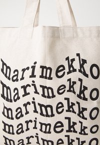 Stofftasche aus beigem Material mit auffälligem, schwarzem Text, der das Wort "marimekko" in verschiedenen schrägen Ausrichtungen wiederholt.