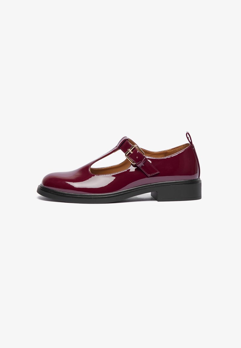 Chaussure Mary Jane en cuir verni bourgogne avec un bout arrondi, une bride T, une boucle ajustable et un petit talon carré. Texture lisse et design simple.