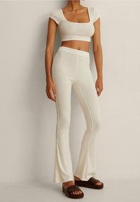Bílý žebrovaný crop top a kalhoty do zvonu, s čtvercovým výstřihem a texturovanou látkou. Doplněno hnědými platformovými sandály.