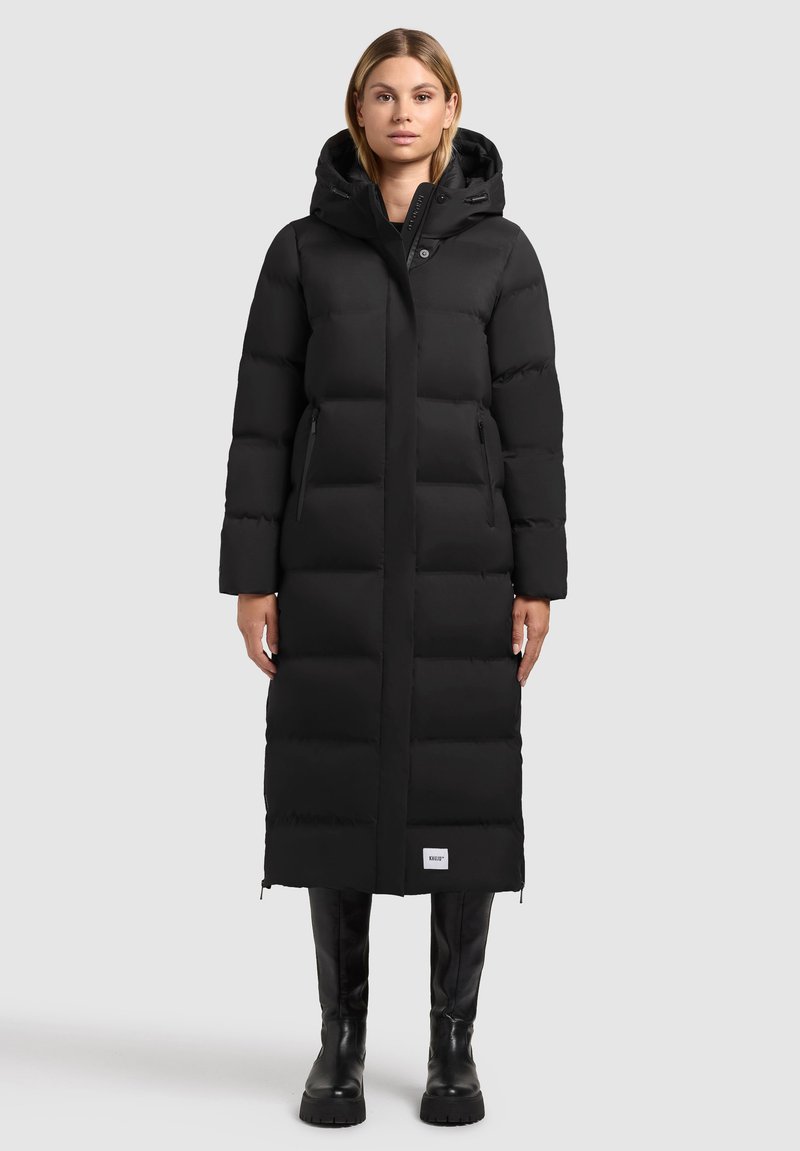 Abrigo largo de plumas negro con un diseño ajustado, capucha y bolsillos laterales con cremallera. Patrón acolchado texturizado y un parche con el logo en el dobladillo.