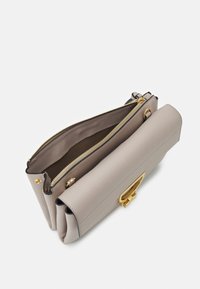 Beżowa torebka skórzana z fakturą, z złotym zapięciem i suwak, pokazana częściowo otwarta z widocznymi trzema przegrodami na białym tle.