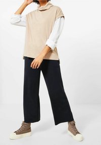 Beige cowl neck top paired with black wide-leg trousers and brown high-top sneakers with cream soles. Smooth fabric and relaxed fit.