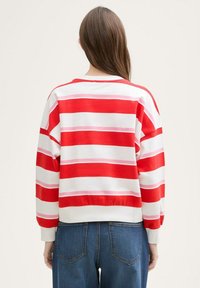 Majica na crveno-bijele pruge s ružičastim detaljima, širokog kroja, okruglog izreza, s rebrastim manžetama i rubom. Vidljiv detalj šivanja na leđima.