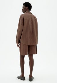 Brown striped shirt and matching shorts, made from lightweight fabric. Features a relaxed fit, collar, and slip-on gray shoes.
